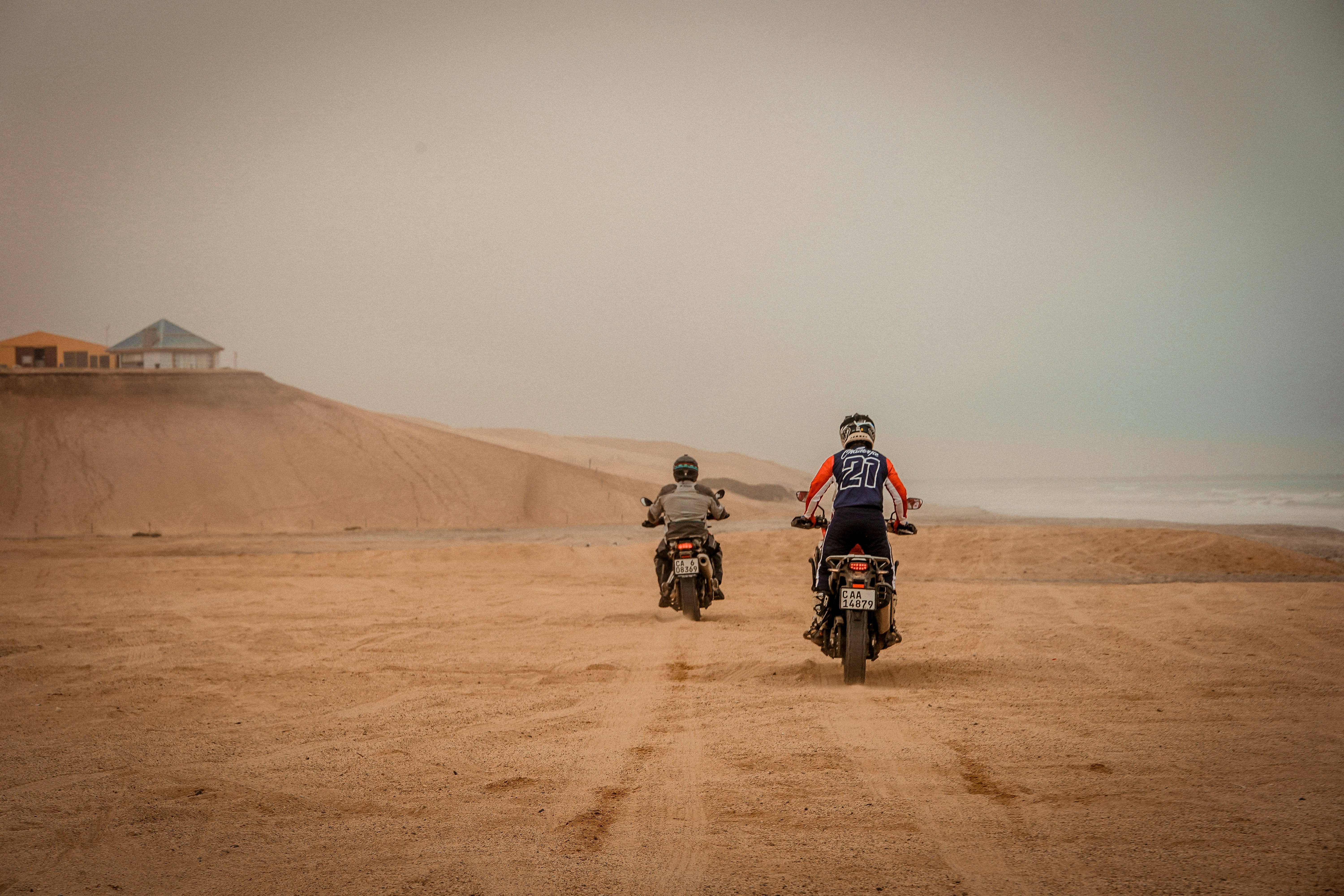 2 men riding motorcycle on brown sand during daytime